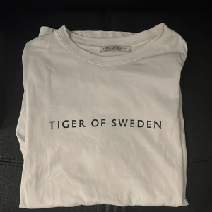 Vit t-shirt från Tiger of Sweden - Vit t-shirt från Tiger of Sweden med klassisk rund hals och svart logotyptryck framtill. Strlk M