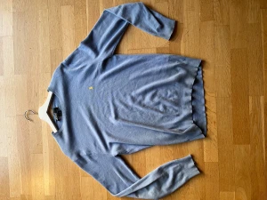 Ljusblå tröja från Polo Ralph Lauren - Snygg ljusblå tröja från Polo Ralph Lauren med klassisk rund hals och lång ärm. Tröjan har en liten gul broderad logga på bröstet och är gjord i mjuk bomull. Perfekt för dig som gillar stilrena och tidlösa plagg.