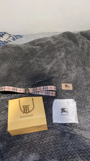 Burberry bälte rutigt & svart - Två snygga Burberry-bälten säljes! Ett klassiskt rutigt bälte i beige, rosa och svart med silverfärgat B-spänne, samt ett svart bälte med diskret rutmönster och silverfärgat spänne. Båda i skinn och levereras med originalpåse och Burberry-påse.