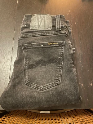 Svarta skinny jeans från Nudie Jeans - Snygga svarta jeans från Nudie Jeans med klassisk femficksdesign och orangea detaljer vid bakfickan. Modellen är skinny med smal passform och raka ben. Jeansen har låg midja och är tillverkade i mjukt denim-material för en bekväm känsla.