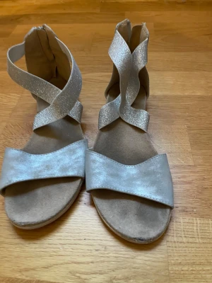Silvriga sandaler med glittriga band - Snygga sandaler i silver med glittriga korsade band över foten och öppen tå. Sulan är platt och har räfflat mönster undertill för extra grepp. Perfekta för sommarens alla äventyr och ger en cool touch till din outfit.