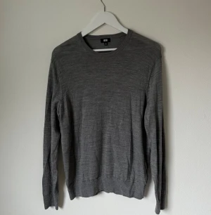 Grå ulltröja från Uniqlo - En stilren grå tröja från Uniqlo i 100% ull. Tröjan har rund halsringning, långa ärmar och en klassisk passform. Perfekt för lager-på-lager och enkel att matcha med olika outfits. 5K11