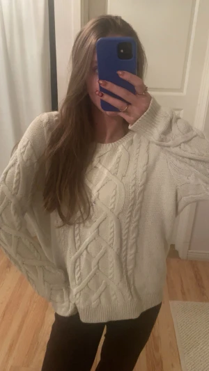 Vit stickad tröja med flätmönster - Säljer en vit stickad tröja med grovt flätmönster och ribbade muddar. Tröjan har en loose passform och kan bäras offshoulder för en chill vibe. Perfekt för dig som gillar mysiga och stilrena plagg med lite extra struktur.