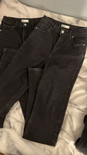 Svarta jeans från Gina Tricot, strl 34 - Säljer ett par svarta jeans från Gina Tricot i storlek 34. Klassisk femficksmodell med utsvängda ben och normal passform. Jeansen har knapp och dragkedja framtill samt bälteshällor. Perfekt basplagg för garderoben.