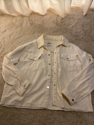 Vit vårjacka - Säljer en vit jacka från Zara i strl S. Perfekt inför våren. Jackan har långa ärmar, två bröstfickor med knappar och silverfärgade tryckknappar framtill. Ganska använd och har små fläckar men inget man tänker på skulle jag säga💞