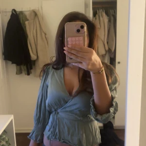 Grön omlottblus från Pigalle XS - Snygg ljusgrön omlottblus från Pigalle i storlek XS. Blusen har långa ärmar med rynkade muddar, v-ringning och knyt i midjan för en feminin siluett. Tillverkad i ett mjukt och lätt material som ger en skön känsla. Perfekt för dig som gillar trendiga detaljer. Nypris 399kr