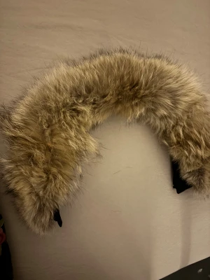 Canada goose päls - Canada goose jacka päls, ett fluffigt diadem med beige och bruna nyanser av päls. Insidan är svart och har en mjuk, böjd form som sitter skönt runt huvudet. Perfekt för dig som vill sticka ut med en cool accessoar och addera lite extra värme till din look.