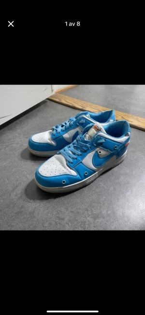 Nike Dunk Low Off-White blå/vit - Nike Dunk Low Off-White sneakers i blått och vitt med klassisk snörning och perforerad tå. Skorna har tydliga Off-White detaljer och text på sidan, samt en platt sula och rund tå. Materialet är syntet och skinn, med en fräsch och sportig vibe.