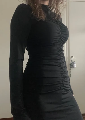Svart klänning - En svart figurnära och kortare klänning med draperad eller rynkat mönster där framme och på sidorna. Den har en mindre turtleneck, materialet är stretchigt och bekvämt. Knappt använd så nyskick gäller!🙌