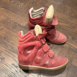 Röda Isabel Marant wedge sneakers bekett - Coola röda bekett sneakers från Isabel Marant i mocka och skinn. Skorna har tre kardborreband, hög plös och vadderad insida för extra komfort. Snygg gummisula och unik design som sticker ut. Perfekta för dig som vill ha en statement-sneaker med höjd. Använda men väl omhändertagna. 
