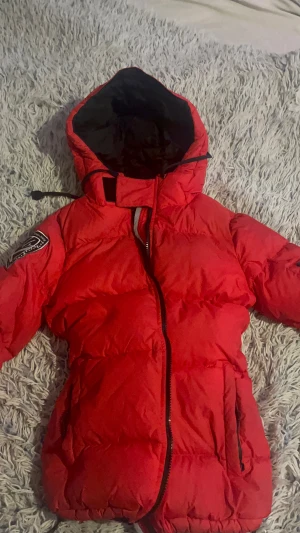 Röd pufferjacka XS - Säljer en röd pufferjacka i storlek XS. Jackan har huva, svart innerfoder, dragkedja framtill och en snygg patch på ärmen med texten 'Swedish Design Since 2006'. Perfekt för kalla dagar och riktigt skön att bära. skicka gärna prisförslag om ni har! btw jag postar alltid samma dag eller dagen efter!