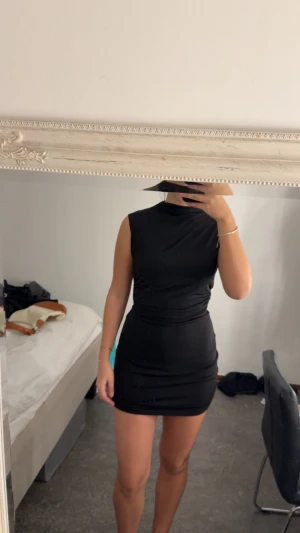 Svart tight ärmlös kortklänning - Säljer en svart, tight och ärmlös kortklänning med hög hals. Klänningen har en figurnära passform och snygga draperingar i midjan som ger en smickrande siluett. Perfekt för dig som gillar en stilren och enkel look.