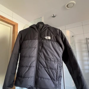 Svart pufferjacka från The North Face - Säljer en svart pufferjacka från The North Face med huva och dragkedja framtill. Jackan har en stilren look med diskret logga på bröstet och en bröstficka med dragkedja. Perfekt för kalla dagar och enkel att matcha med allt.kan vara i två olika färger som ni ser på bilderna.För mer frågor eller funderingar kontakta mig😃
