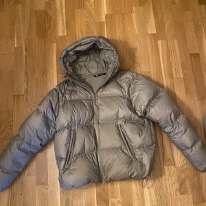 Beige pufferjacka från Zara x All caps studio - Säljer en snygg beige pufferjacka med dun från Zara med huva och dragkedja framtill. Jackan har två fickor med dragkedja och justerbar dragsko nedtill. Varm och skön att bära under vintern. Köpte den för 1300kr men säljer för mindre. Har någon mini fläck men inget stort. (Zara 100% FEATHER FILL PUFFER JACKET X ALL CAPS STUDIO)