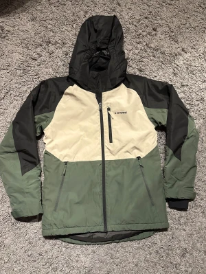 Grön och svart skidjacka från Everest - Säljer en snygg skidjacka från Everest i färgerna grön, svart och beige. Jackan har huva, dragkedja framtill och flera praktiska fickor med dragkedja. Perfekt för dig som gillar outdoor och vill ha en jacka med cool färgblockad design. Varm och skön! Mycket bra skick. 