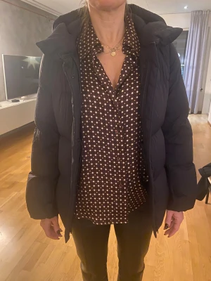 Svart pufferjacka med huva - Säljer en svart dunjacka  med stor, mysig huva och quiltad design. Jackan är från Uniqlo och använd ett fåtal gånger.