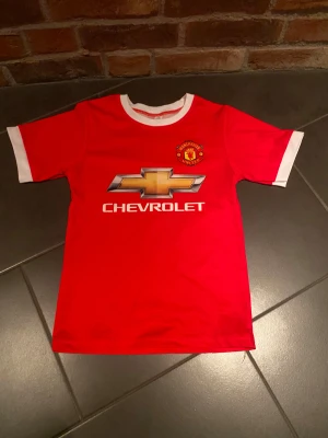 Manchester united T-skirt - Hej, säljer min gamla Manchester United T-skirt som nu är för liten. Den är helt i tyg och inget tryckt plast på. Storleken är 140.