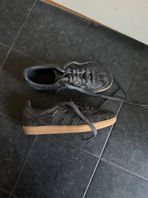 Adidas Samba Og W i nyskick - Säljer ett par Adidas Samba sneakers i svart med snyggt snakeskin-mönster och klassiska tre ränder på sidan. Storlek 38. Passar mig som har skostorlek 37. Endast använda 3 gånger