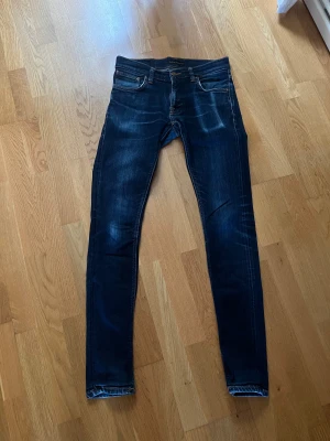 Nudie Jeans Tight Terry W30 L34 - Säljer ett par mörkblå Nudie Jeans Tight Terry i modellen Dry Deep Orange. Jeansen har skinny/slim passform, klassiska fem fickor och snygga orangea sömmar. Materialet är 99% ekologisk bomull och 1% elastan för extra stretch. Perfekta för dig som gillar en tajt slim fit look. Köpta för 1500 farsans gamla 