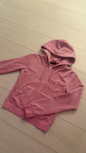 Rosa velour hoodie Juicy Couture XS - Säljer en ikonisk rosa hoodie från Juicy Couture i mjuk velour. Tröjan har huva, dragkedja med J-detalj, fickor fram och broderad logga på bröstet. Perfekt för dig som vill ha den där klassiska Y2K-looken. Nypris 1200kr