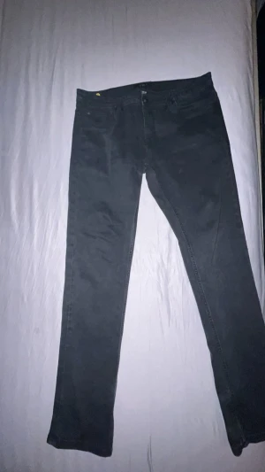 Svarta jeansbyxor från SMOG 34/34 - Svarta jeansbyxor från SMOG i klassisk femficksmodell. Raka ben och normal passform, midwaist. Snygga och stilrena med knapp och dragkedja framtill. Perfekta för dig som gillar enkel och clean look.