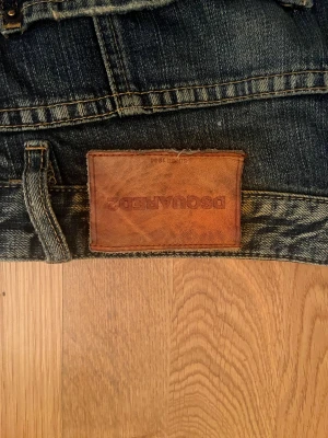 Dsquared2 jeans med färgstänk - Snygga blå jeans från Dsquared2 med coola färgstänk i vitt och orange, slitna detaljer och patch på bakfickan. Jeansen har raka ben och klassisk femficksdesign. Perfekt för dig som gillar streetstyle och vill sticka ut. Helt äkta.