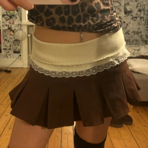 Brun plisserad minikjol med spetskant - Supersöt brun plisserad minikjol med bred ribbad midja i vitt och dekorativ spetskant. Köpt i thailand och är stretchigt material, så passar xs-m, aldrig använd