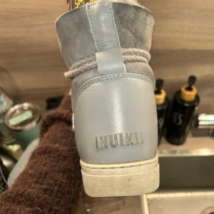 Grå boots från Inuikii  - Säljer ett par snygga grå boots från Inuikii med grov snörning och mjuk päls på insidan. Skorna har en platt sula och är tillverkade i en mix av mocka och skinn, vilket ger dem en lyxig och mysig känsla. Perfekta för kalla dagar och riktigt stilrena.