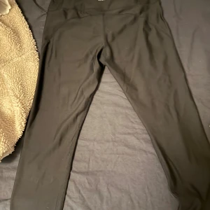 Svarta leggings med hög midja - Svarta leggings med hög midja och tight passform. De är tillverkade i ett stretchigt syntetmaterial som sitter skönt mot kroppen. Perfekta för träning eller chill dagar. Snygg och enkel design utan synliga loggor eller detaljer.