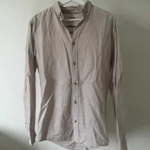 Beige skjorta från Jack & Jones - Snygg beige skjorta från Jack & Jones Essentials, perfekt för sommaren. Skjortan har klassisk button down-krage, långa ärmar och knappar framtill. Tillverkad i en skön mix av bomull och linne som ger en lätt och luftig känsla. Enkel och stilren design som funkar till många outfits. Modellen är 180cm