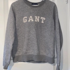 Grå sweatshirt från GANT - Säljer en klassisk grå GANT sweatshirt med vit text på bröstet. Den är i storlek M, men passar även bra för dig som har XS/S om du vill ha en mer avslappnad och loose fit. Perfekt för en stilren men bekväm vardagslook.  Vänligen läs min bio innan du gör ett köp; där hittar du bland annat information om leveransprocessen med mera 😊