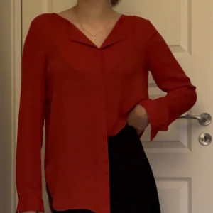 Röd långärmad skjorta - Snygg röd skjorta med v-ringad hals och långa ärmar. Skjortan har en loose passform och är tillverkad i ett lätt, flowy material som ger en skön känsla. Perfekt för dig som gillar stilrena plagg med enkel design.