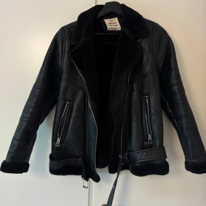 Svart teddyjacka från ZARA girls - Säljer en svart teddyjacka från ZARA girls med mjukt foder, stora slag och dragkedjor framtill. Jackan har bälte i midjan och detaljer i fuskpäls vid ärmslut och nederkant. Perfekt för kyliga dagar och ger en cool look.