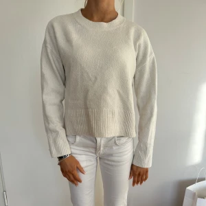 Vit stickad tröja från & Other Stories - Superfin vit stickad tröja från & Other Stories med rund halsringning och breda ribbade muddar vid ärmslut och nederkant. Tröjan har en klassisk, rak passform och är perfekt för lager-på-lager under kyliga dagar.