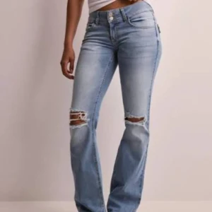 Blå bootcut jeans med slitna knän - Snygga ljusblå jeans med bootcut passform och slitna detaljer vid knäna. Klassisk femficksmodell med knappstängning och bälteshällor. Jeansen har en normal midja och är tillverkade i mjukt denimtyg som ger en avslappnad vibe. Jag är 162, uppsydda enligt alla mina bilder förutom. De går till marken på mig. Några trådar har gått upp vid knappen