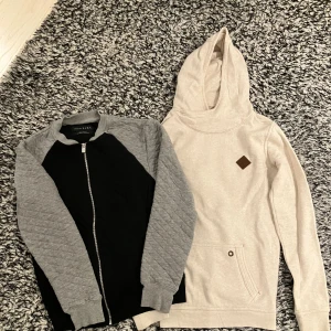 Beige hoodie från Cube Co & quiltad kofta Zara - Säljer en beige hoodie från Cube Co med huva och magficka samt en svart och grå quiltad kofta från Zara Essentials med dragkedja. Hoodien har en stilren look med brunt märke på bröstet och koftan har grå ärmar och svart kropp. 170cm. 