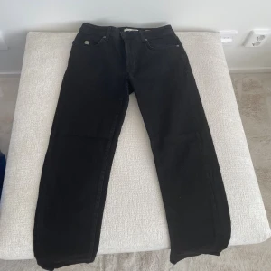 Svarta raka jeans - Svarta jeans med klassisk femficksdesign och raka ben. Jeansen har en enkel look utan synliga slitningar eller detaljer, perfekt för en clean och stilren outfit. Passar dig som gillar en tidlös och enkel stil.