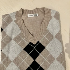 Beige och svart rutig tröja  - Snygg stickad tröja från Shein med klassiskt rutig argylemönster i beige, svart och grått. Tröjan har v-ringad halsringning, ribbade muddar och långa ärmar. 