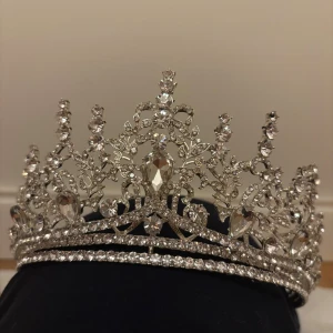 Glittrande silverfärgad tiara - En riktigt maffig tiara i silverfärg med massor av gnistrande stenar och detaljerade blommönster. Tiaran har en klassisk, kunglig form med höga spetsar och stora kristalliknande stenar som fångar ljuset. Perfekt nu inför Halloween.