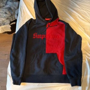 Supreme tvåfärgad hoodie M - Supreme hoodie i svart och rött med broderad Supreme-logga på bröstet. Tröjan har huva med snörning, känguruficka och är tillverkad i mjuk bomull. Snygg tvådelad design som sticker ut och passar perfekt till alla!! 