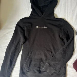 Svart hoodie från Champion M - Svart hoodie från Champion i storlek M. Klassisk modell med huva, magficka och Champion-logga broderad på bröstet. Mjuk och skön bomullsblandning. Snöret är borta