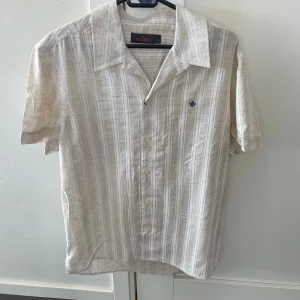 Randig kortärmad skjorta från Morris - Säljer en helt ny randig vit beige Morris skjorta i storlek M. Skjortan är kortärmad. Hör av dig vid funderingar!