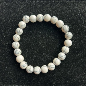 Vitt pärlarmband med marmormönster - Snyggt armband med runda vita pärlor som har grå marmormönster. Elastiskt band gör det enkelt att ta på och av. Perfekt accessoar för att ge din outfit en clean och stilren touch.