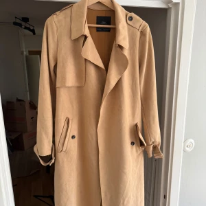 Beige trenchcoat från Zara, strl S - Snygg beige trenchcoat från Zara med klassisk krage, knappar och bälte i midjan. Jackan har långa ärmar med spännen vid handlederna och två fickor framtill. Perfekt för dig som vill ha en stilren och tidlös look.