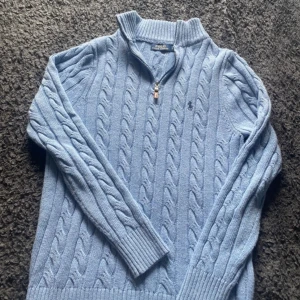 Ljusblå stickad tröja Polo Ralph Lauren - M - Kabelstickad ljusblå tröja från Polo Ralph Lauren med half zip och krage, bra kvalite sömen på armen är lite uppe men inget som syns eller känns. Den är med som M än L. Slim fit och kroppsnära