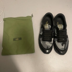 Valentino Rockrunner sneakers svart/grå - Snygga Valentino Rockrunner sneakers i svart och grått med camouflage-mönster. Skorna har svarta snören, detaljer i mocka och mesh samt coola nitar på hälen. Kommer med original grön dustbag och även extra skosnören
