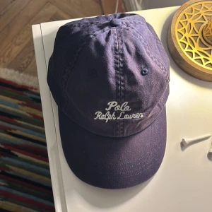 Mörkblå keps från Polo Ralph Lauren - Snygg mörkblå keps från Polo Ralph Lauren med broderad logga framtill och klassisk polospelare bak. Justerbar rem baktill för perfekt passform. Tillverkad i bomull för en skön känsla och stilren look.