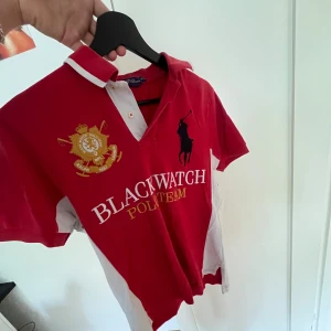 Röd pikétröja Polo Ralph Lauren M - Säljer en röd pikétröja från Polo Ralph Lauren med broderad logga, stora tryck och detaljer i vitt och gult. Klassisk krage med vita inslag, kort ärm och nummer 3 på ärmen. Modellen är custom fit och har tydlig Blackwatch Polo Team-brodyr. Står storlek M men den var för liten för mig så den är mer åt S hållet. Har aldrig använt den.