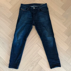 Mörkblå Diesel jeans, storlek 30 - Snygga mörkblå jeans från Diesel med klassisk femficksdesign och diskret logga på fickan. Modellen har smal passform och raka ben, tillverkade i stretchigt bomullsmaterial för extra komfort. Perfekt för dig som gillar stilrena och moderna jeans.