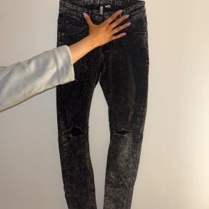 Svarta super skinny jeans H&M Divided - Svarta super skinny jeans från H&M Divided i tvättad look med slitna detaljer vid knäna. Tight passform med låg midja och klassiska fem fickor. Jeansen är i stretchigt material och har en cool, lite grunge känsla.